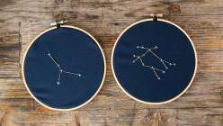 Two Embroidery hoops with dark blue fabric as the base. Constellations are stitched on in gold and silver thread.