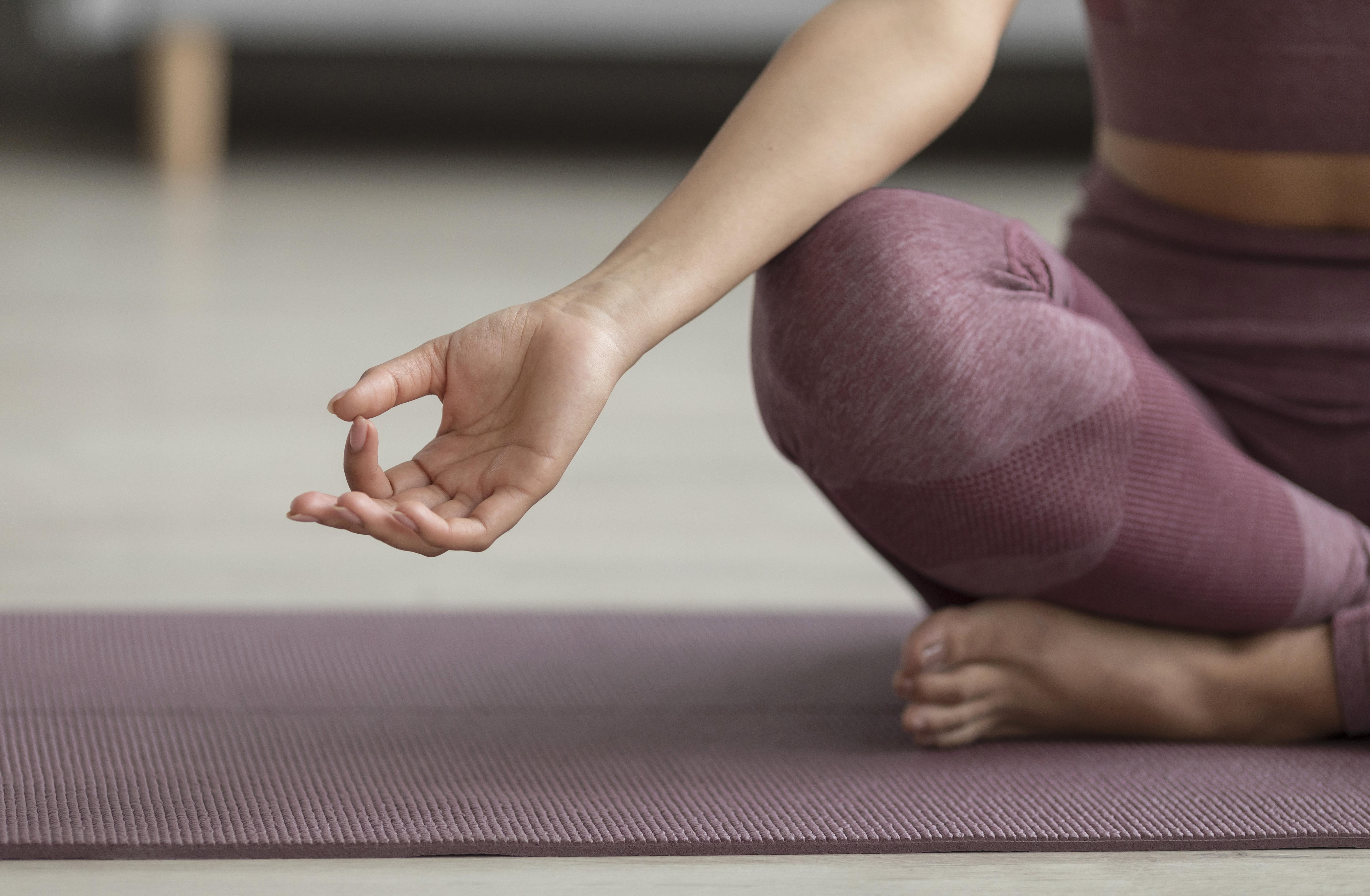 A woman holding a sitting yoga pose on a purple yoga mat. 