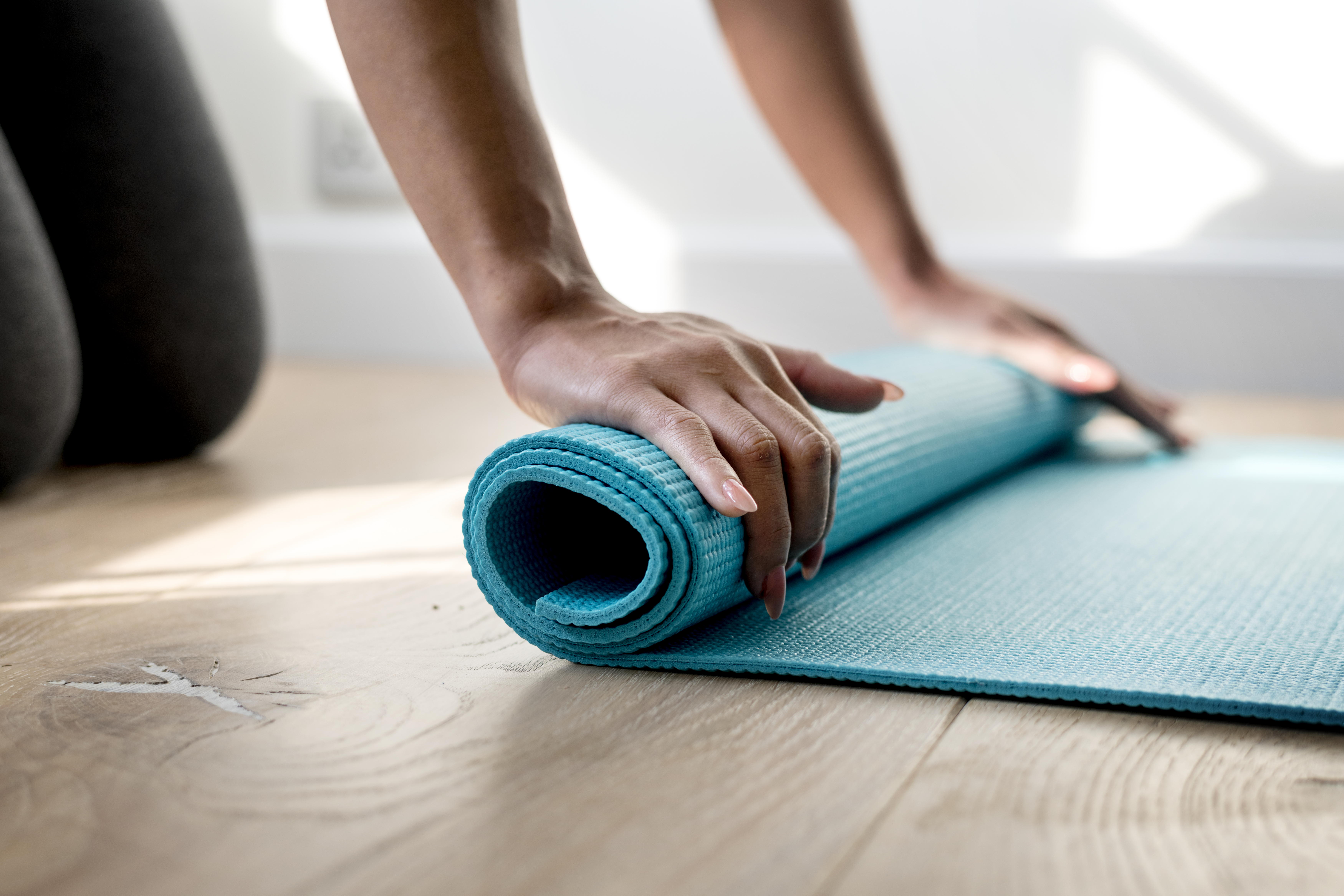 A woman on the floor rolling up a blue yoga mat.