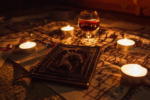 A dark room with a table that has a goblet of wine, candles, a book, and a map.