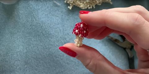 Beaded mushroom in between the fingers of the artist who created it