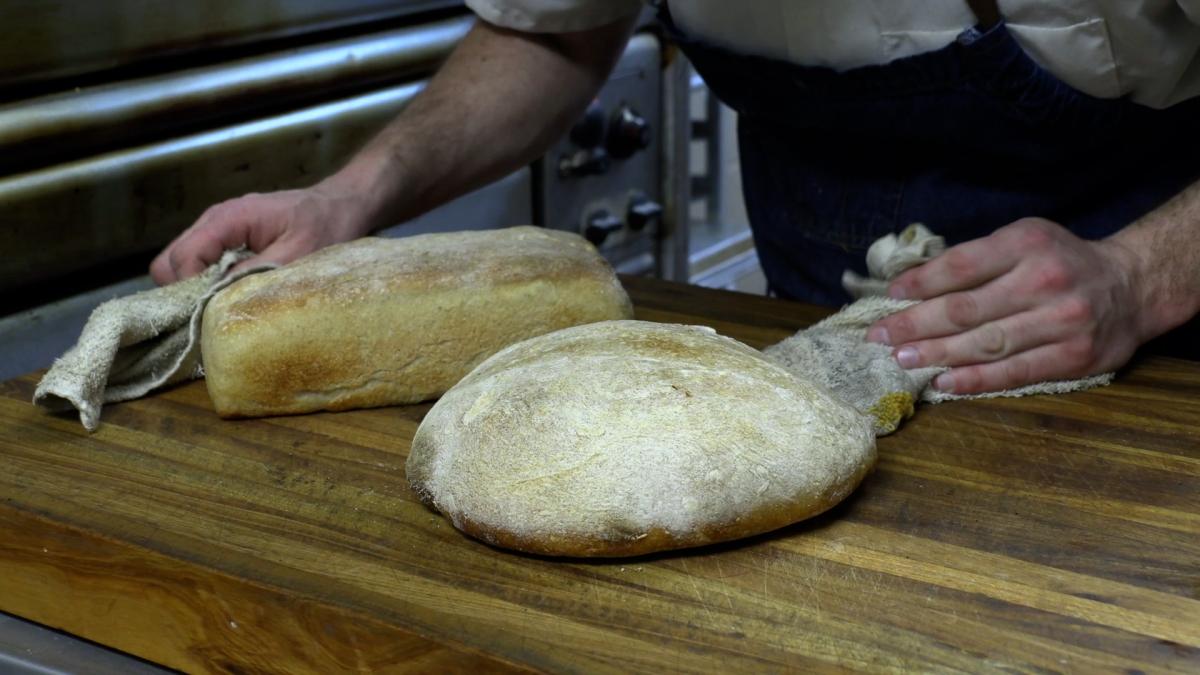 Baker Tyler Gallagher hands alongside two fresh sourdough bread loaves just out of the oven.